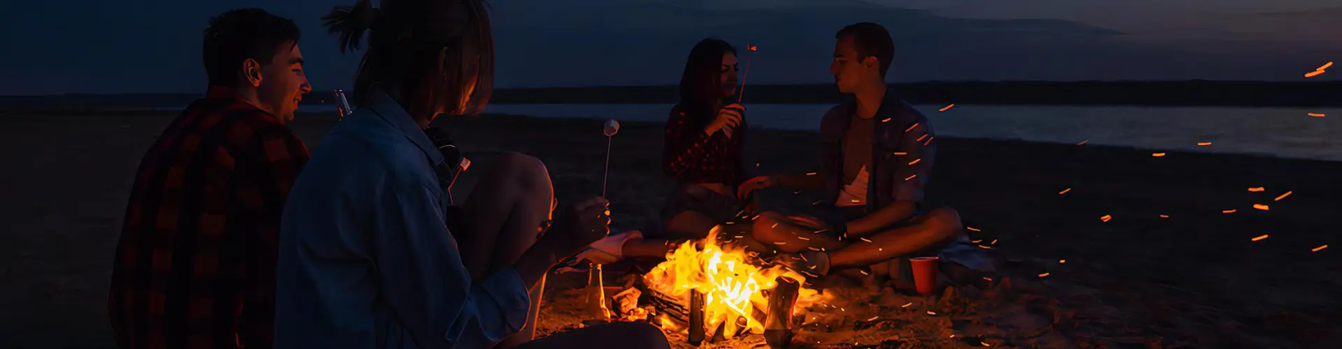 A group of people relaxing around a glowing beach campfire at night enjoying each other’s company in our corporate showcase tour