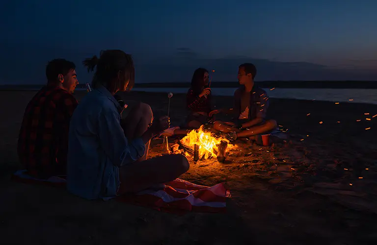 A group of people relaxing around a glowing beach campfire at night enjoying each other’s company in our corporate showcase tour