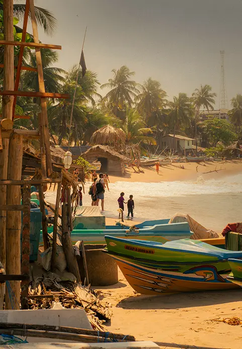 A lively coastal scene with bright fishing boats, rustic huts, and tall palm trees, representing the charming local beach villages you can visit on Eastern Blues Tour