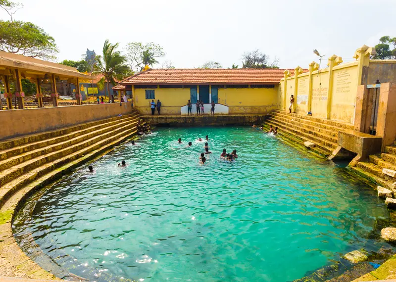 Historic stone stepped hot spring pool with clear turquoise water and locals
