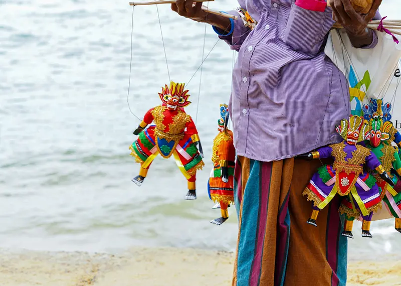 Local vendor selling bright traditional mask string puppets on a sandy beach