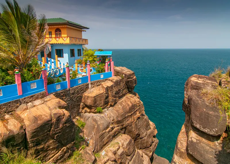 A brightly colored building surrounded by a bright blue wall perched on the edge of a rugged rocky cliff overlooking a vast, deep blue ocean, a breathtaking scenic view you can discover on our custom Sri Lanka tours