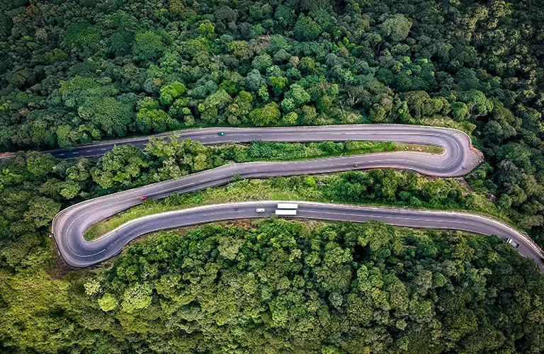 A top-down view of vehicles navigating a curved mountain highway surrounded by lush jungle, highlighting the picturesque travel routes you will experience on custom Sri Lanka tours