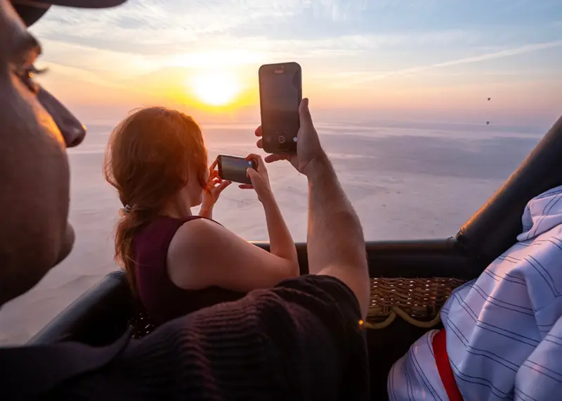 A couple takes phone pictures of the sunrise during a balloon safari