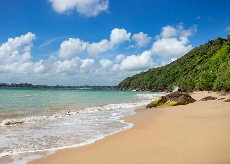 Calm ocean waves washing onto a pristine sandy beach near green hills