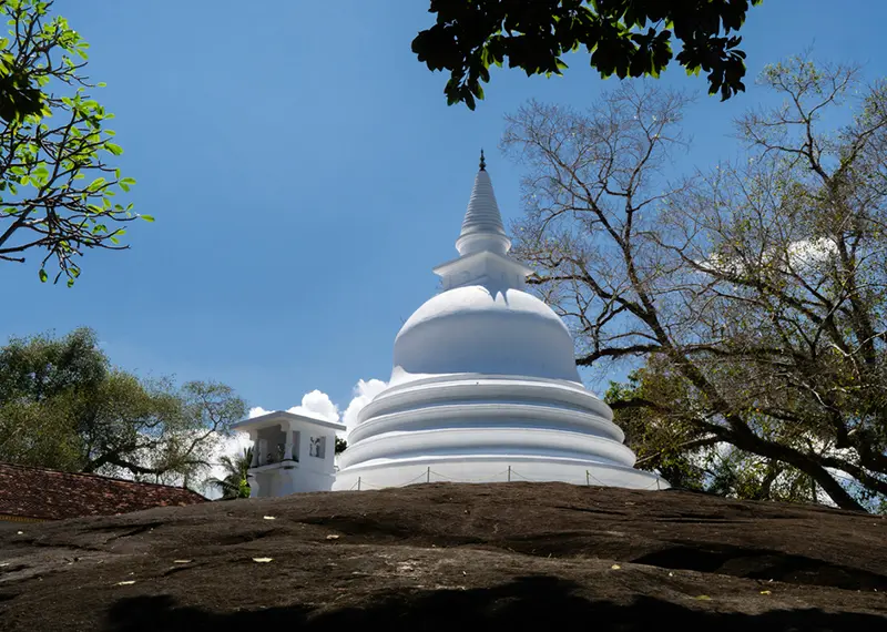 A white Buddhist stupa situated on a large natural dark rock formation