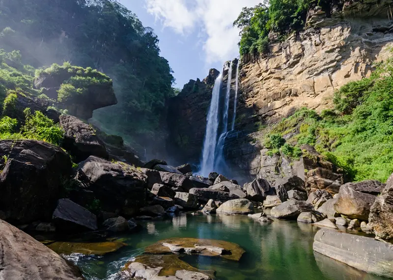 Scenic tropical waterfall surrounded by large boulders and lush green nature trails