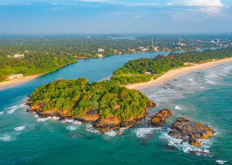 Aerial view of a forested headland surrounded by sandy beaches and ocean