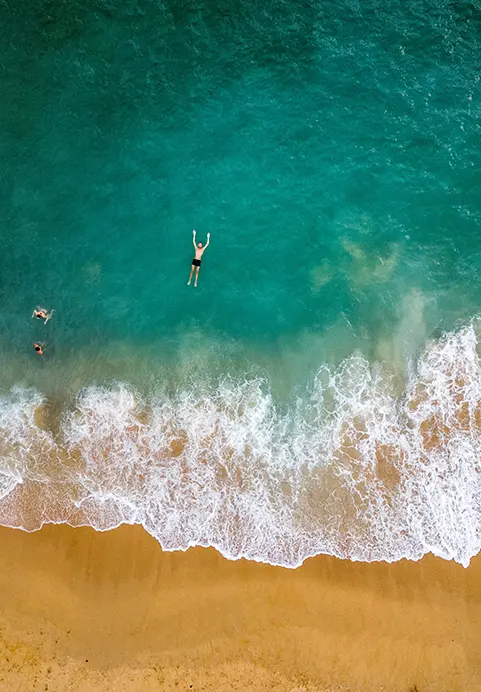 A top-down shot of a traveler swimming in beautiful emerald sea water next to crashing waves, representing the tranquil beach destinations you can enjoy on Southern Sands Voyage Sri Lanka tour.