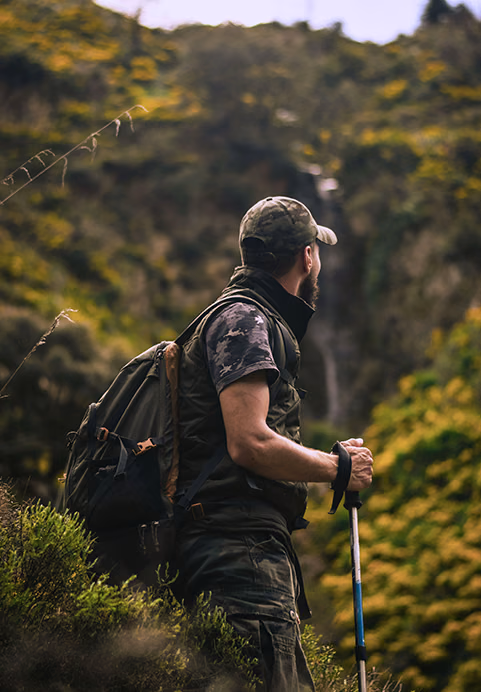 A male hiker with a backpack and trekking poles looking out over lush green mountains during a guided trekking adventure on a private Sri Lanka tour