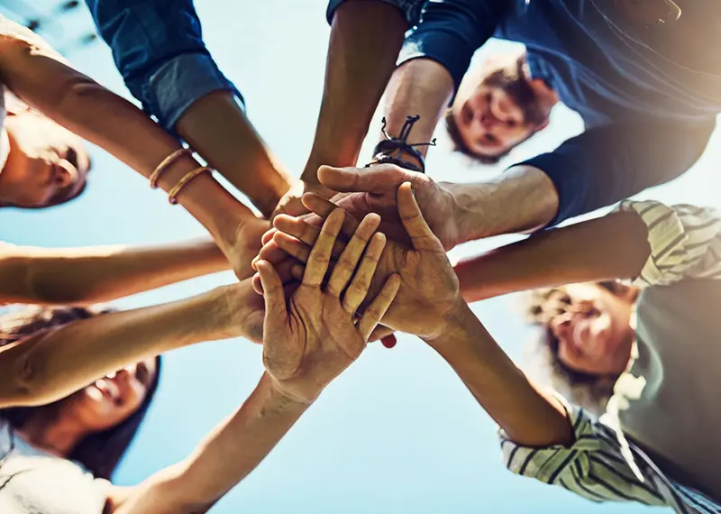 A diverse group of people stacking their hands together in unity outdoors