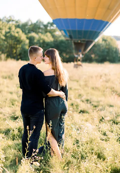 A couple embracing in a sunlit grassy field with a hot air balloon in the background during a romantic Enchanting Sri Lanka - A 17 Day Bespoke Honeymoon Odyssey tour