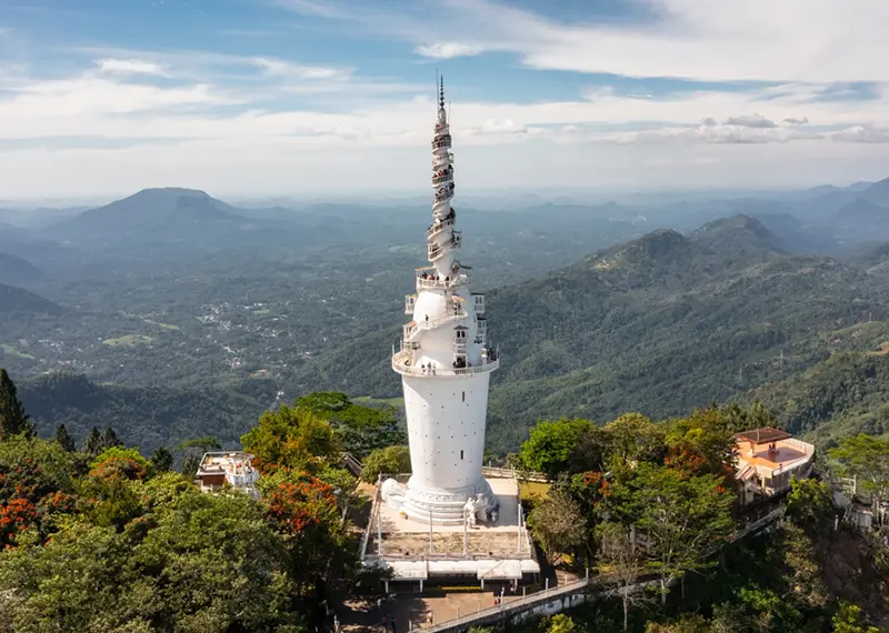 A tall white spiraling tower stands on a lush green mountain peak