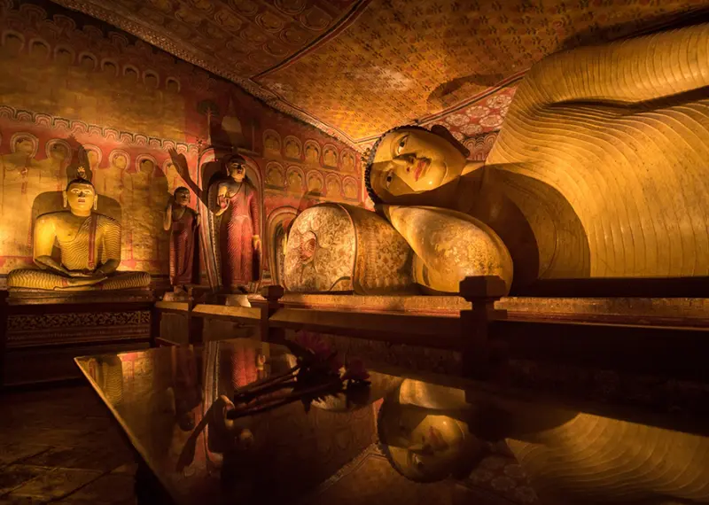 Golden reclining Buddha statue inside a historic and beautifully painted cave temple