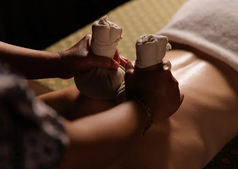 A therapist applies warm herbal compresses to a relaxing client's bare back