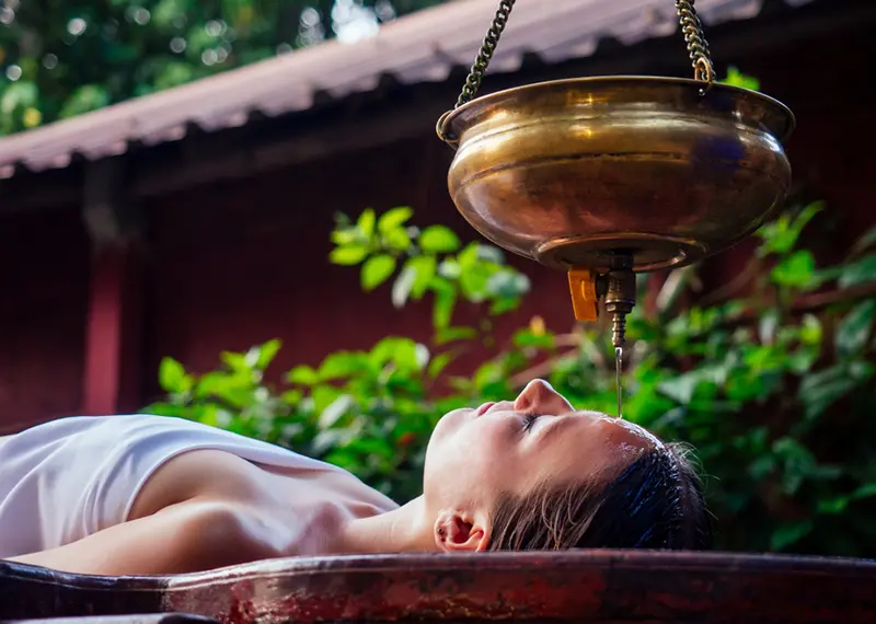 A relaxed woman receives a traditional Ayurvedic oil treatment on her forehead