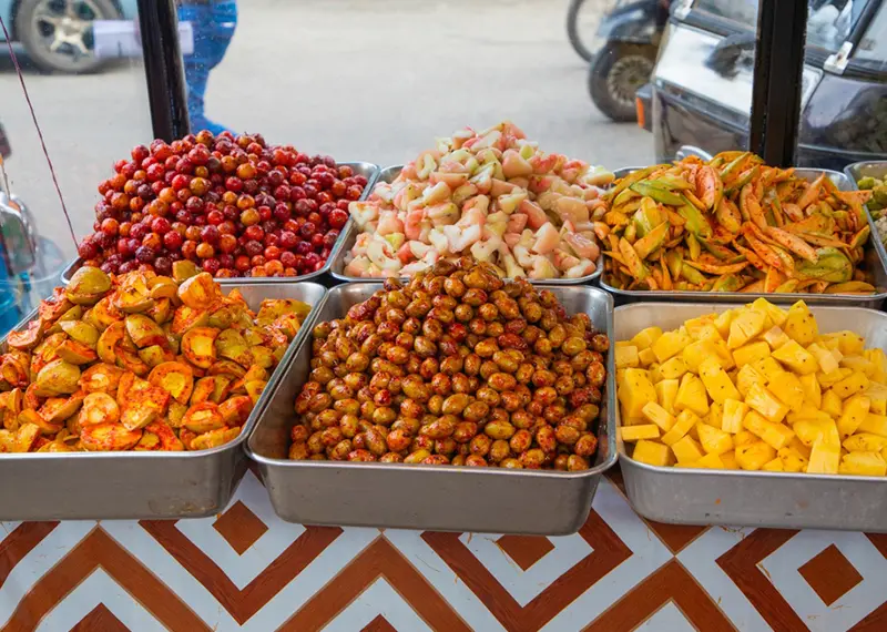 A colorful display of spicy pickled fruits sits at a street stall