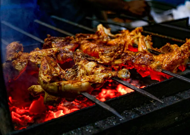 Marinated chicken skewers roast over glowing red coals at a street market