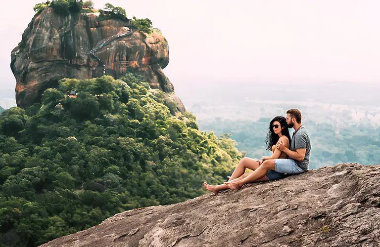 A couple sitting on a rocky cliff enjoying a breathtaking panoramic view of the ancient Sigiriya Lion Rock, highlighting the romantic destinations included in our Sri Lanka honeymoon tour packages