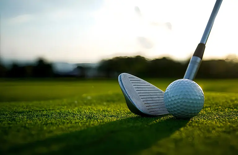 A close-up of a golf club and ball on a lush green course at sunset, highlighting the premium golfing holidays included in our Sri Lanka golf tour packages