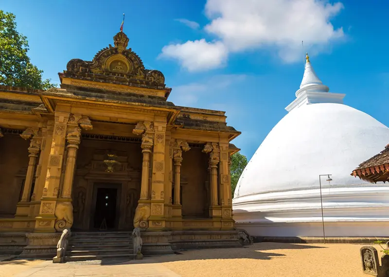 An ornate temple building stands beside a large white Buddhist stupa dome