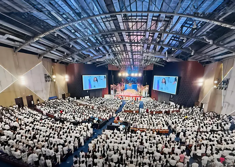 A large crowd dressed in white fills a modern indoor auditorium hall