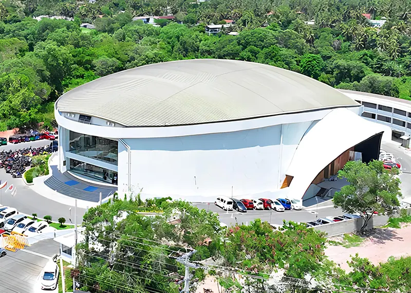 A large white indoor stadium venue surrounded by parking and green trees