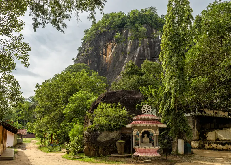 Massive rock mountain towering over a beautiful Buddhist shrine and green trees
