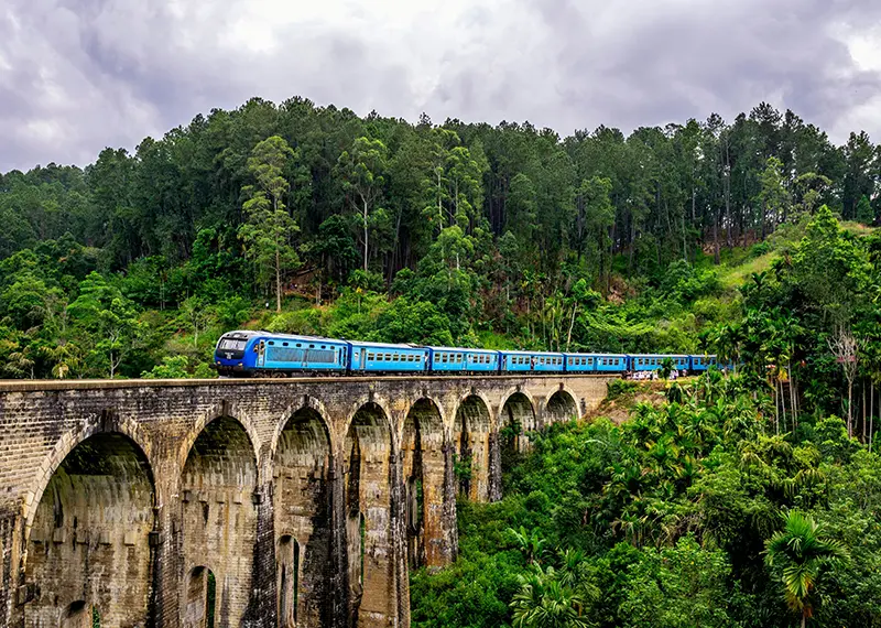 A blue train crossing the historic Nine Arch Bridge in Ella, Sri Lanka