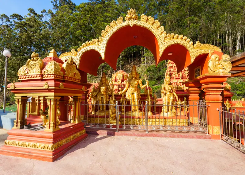 Golden statues of Hindu deities stand within a bright red ornate temple shrine