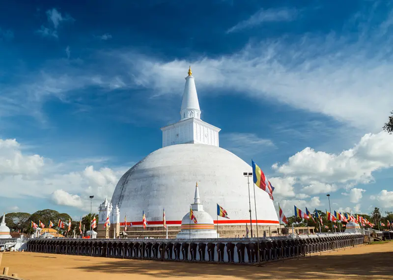 Massive white Ruwanwelisaya stupa with elephant statues and flags in Anuradhapura, Sri Lanka