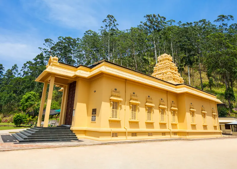 A beautiful golden Hindu temple nestled against a lush forested mountain backdrop
