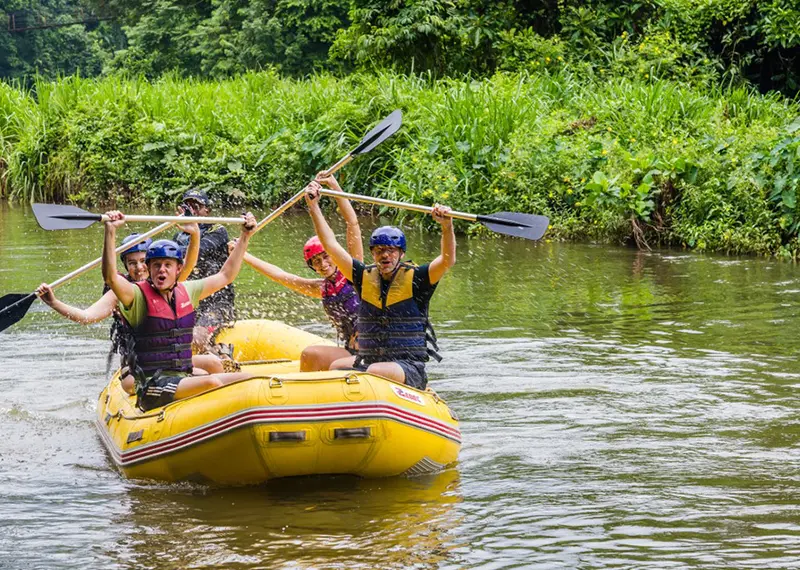 A group of people whitewater rafting down a scenic tropical river together
