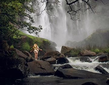 A solo female traveler taking in the scenic views of a large waterfall deep in the jungle during her Sri Lankan tour
