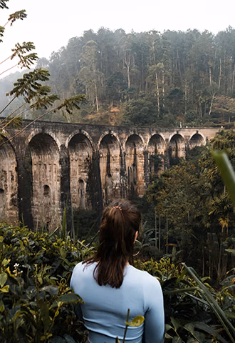 A woman enjoying a secluded viewpoint of a historic stone railway bridge nestled in the hill country during her custom Sri Lanka tour