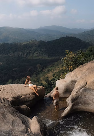 A couple relaxing by a natural hilltop rock pool overlooking a sweeping green mountain valley, a romantic experience perfect for custom Sri Lanka tours