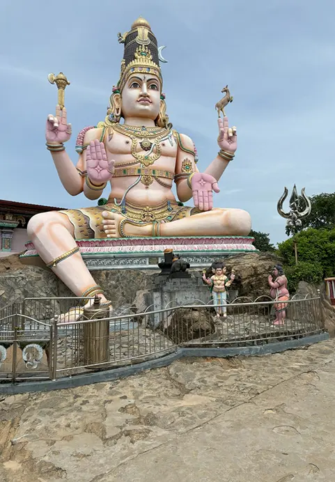 A massive, colorful statue of the Hindu deity Lord Shiva seated on a rocky platform under a bright sky, a prominent religious landmark frequently featured in The Grand Ramayana & Heritage Expedition travel itinerary