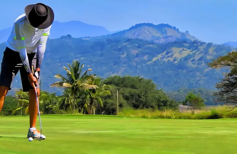 A golfer putting on a scenic green course with a caddie holding the flag and lush blue mountains in the background, a luxury sporting experience available on our The Hill Country Swing tour