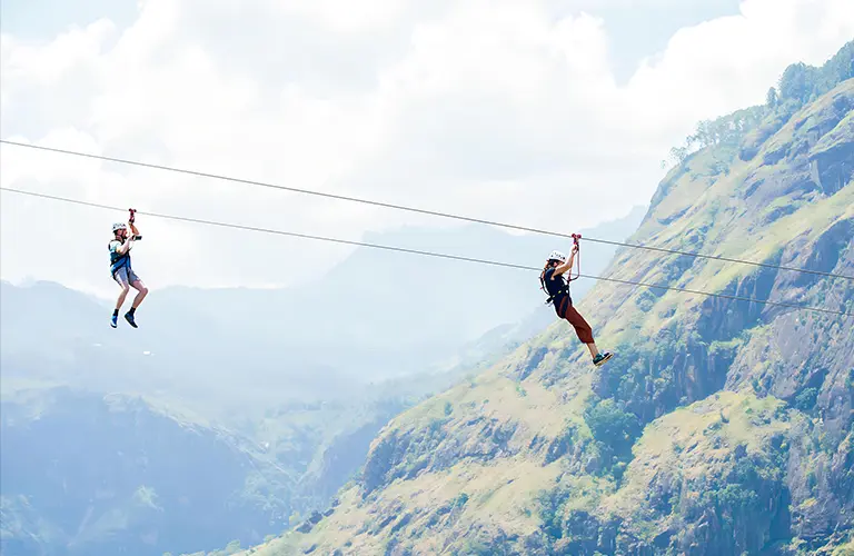 Two adventurous tourists ziplining across a lush green mountain valley in Ella in The Island Pulse - Corporate Event & Adventure Tour