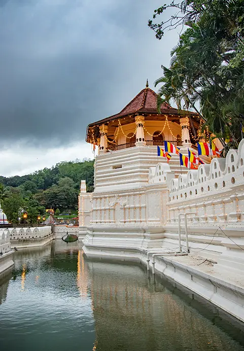 A scenic view of the sacred Temple of the Tooth in Kandy against a dramatic cloudy sky, showcasing the exclusive access to ancient heritage sites available on The Kings & Kingdoms Express tour