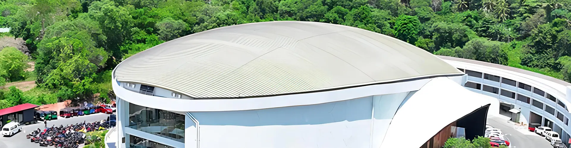 An aerial view of a large, modern dome-shaped white convention center surrounded by lush green trees and parked vehicles, where you can witness spiritual ceremonies and religious customs through The Miracle Dome Spiritual Encounter tour package