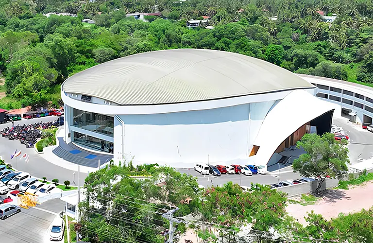 An aerial view of a large, modern dome-shaped white convention center surrounded by lush green trees and parked vehicles, where you can witness spiritual ceremonies and religious customs through The Miracle Dome Spiritual Encounter tour package