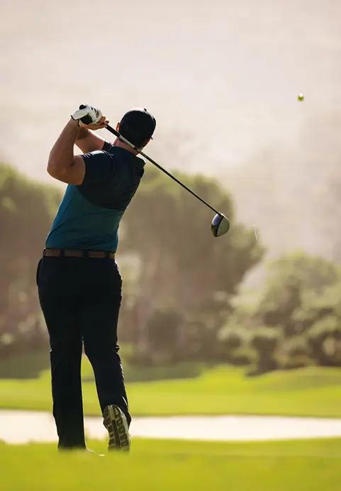 A male golfer finishing his swing on a beautifully manicured, sunlit green golf course with misty trees in the background, a premium sporting experience available through our The Ultimate Sri Lankan Golf Escape tour
