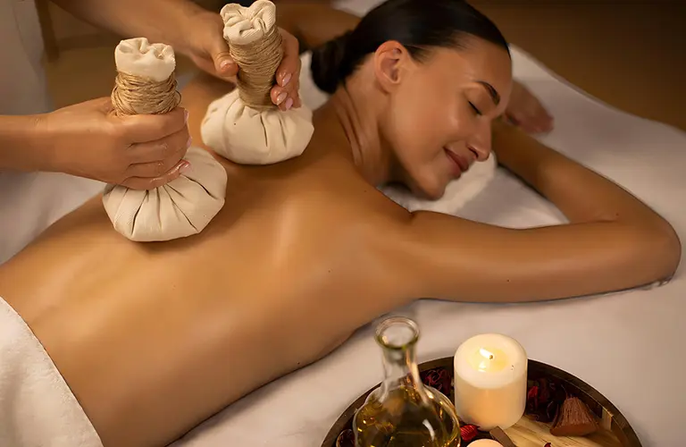A woman relaxing during a traditional Ayurvedic herbal compress massage, a popular wellness experience to include in The Wellness Retreat - An Authentic Ayurvedic Sanctuary tour