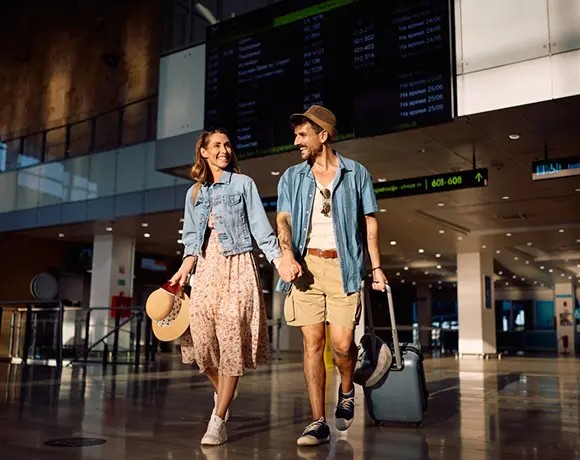 A smiling couple holding hands and walking through an airport terminal with a suitcase, ready to begin their vacation with the seamless airport transfer services included in our Sri Lanka itinerary packages