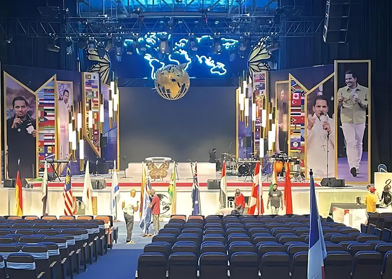A large auditorium stage features international flags and modern event lighting displays