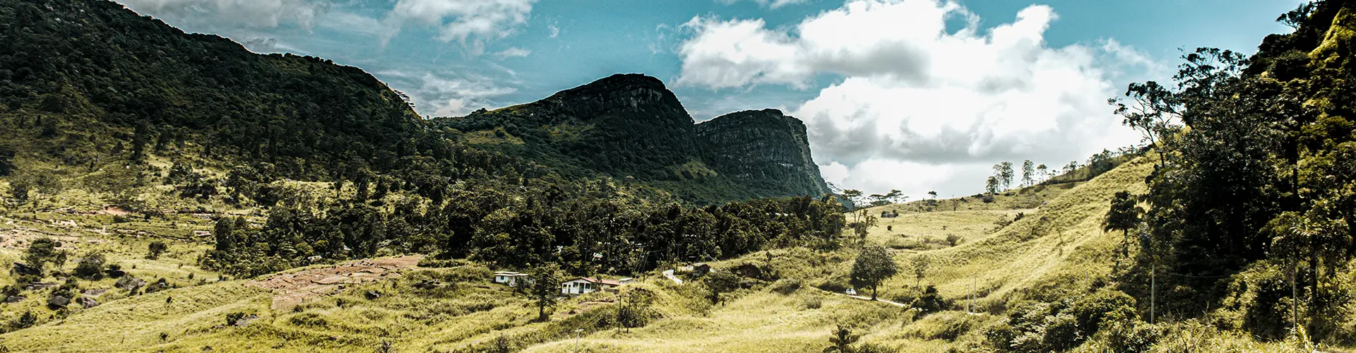 A picturesque view of a rural Sri Lankan valley surrounded by dramatic forested mountains and grassy slopes, representing the beautiful off-the-beaten-path destinations you can explore on Venture Further - The 11 Day Adventure & Wilderness Loop tours.