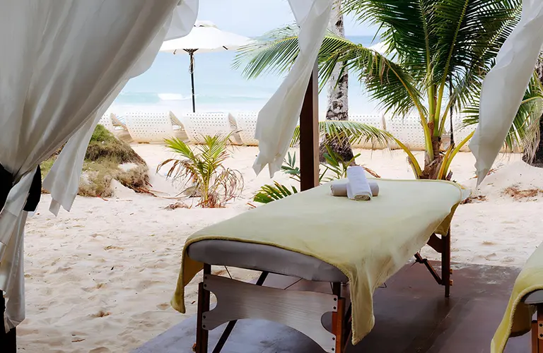 A relaxing outdoor massage table set up on a tropical white sand beach, an idyllic wellness experience to included in Wander & Awaken - The 11 Day Nervous System Reset package